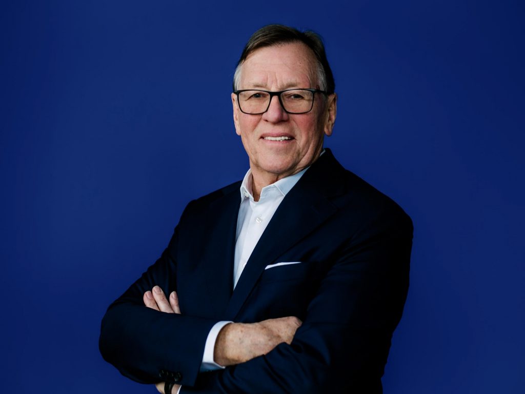 Porträt von Detlef Trenner mit verschränkten Armen vor blauem Hintergrund, Immobilienexperte in Dresden