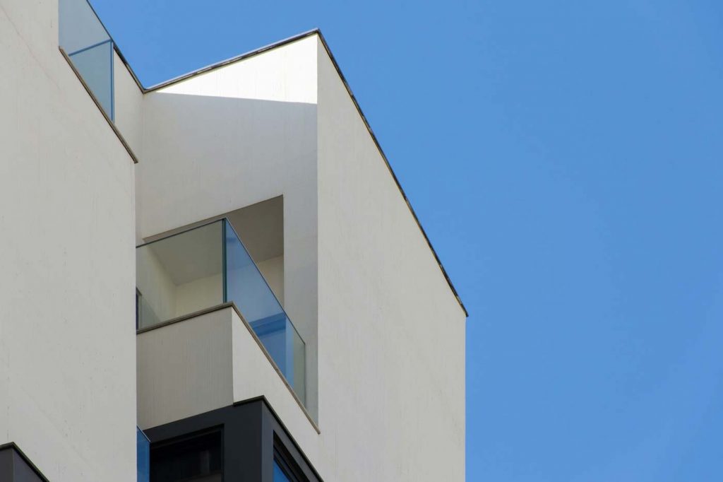 Minimalistische Architektur eines weißen modernen Wohnhauses mit Glasbalkon vor blauem Himmel
