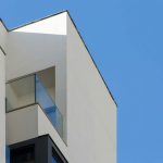 Minimalistische Architektur eines weißen modernen Wohnhauses mit Glasbalkon vor blauem Himmel